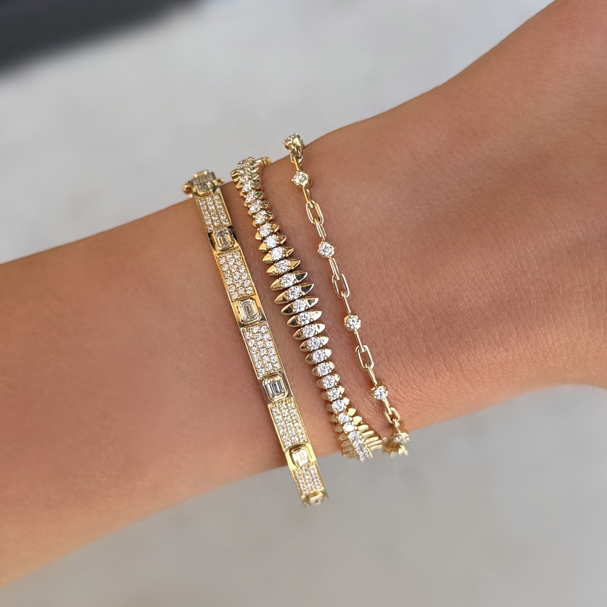Gold bracelets with diamonds on a wrist against a neutral background